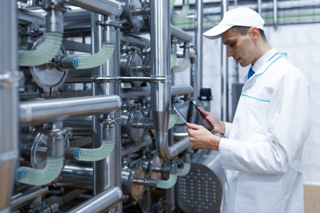 portrait of man in a white robe and a cap standing in production department of dairy factory with grey tablet